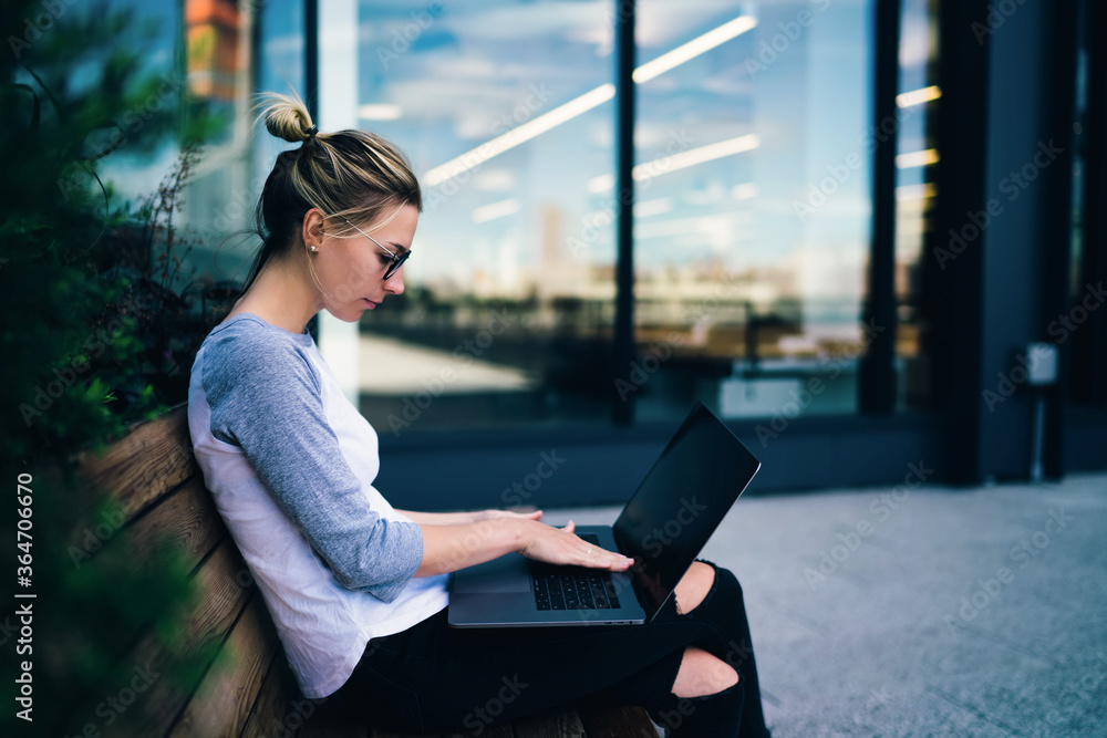 Aufkleber pensive female student keyboarding on netbook searching tutorial while sitting outdoors on bench,hip