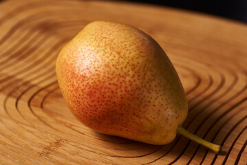 The red-yellow pear lies on a wooden stand on a black background