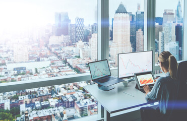 Back view of trader manager sitting at panoramic skyscraper office desktop front PC computer with financial graphs and statistics on screen. Analysis of digital market and investment in block chain