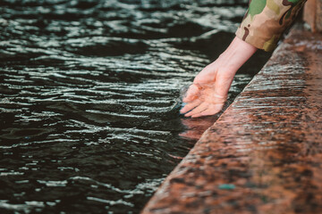 The girl dipped her hand into the water. Touching the river with the palm of your hand while walking along the embankment