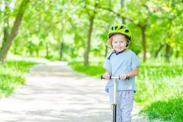 Smiling little girl rides scooter in summer park. Empty space for text