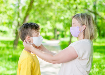 Mother helps put on protective face mask her young son while they are in a public place