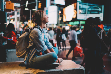 Hipster girl sitting on Times square with smartphone sending photos from landmark at night, female...