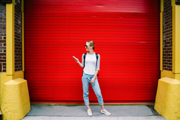 Full length of smiling hipster girl using smartphone standing on urban background near copy space for your advertising,female traveler checking application on mobile phone spending time on street