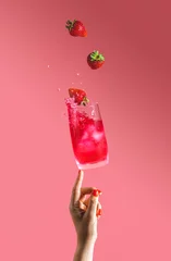 Poster Im Rahmen Woman hand support fly glass of strawberry drink with splash, juice strawberries falling in glass. Summer art food concept on pink background © Victoria Kondysenko