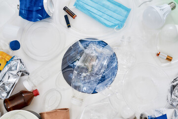 Flatlay composition with different waste, garbage types and paper model of Earth under it in the center over white background