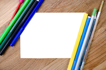 Obraz premium A white sheet of paper on a wooden background and stationery are nearby. Sheet of paper and pencils, felt-tip pens. Mock up