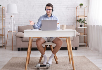 Employee makes a video call with team. Surprised guy in shirt, shorts and socks looks at laptop and...