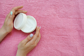 Woman's hands near white jar of face cream on pink background