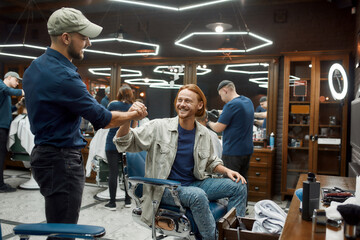 Professional barber and his happy client shaking hands at barbershop