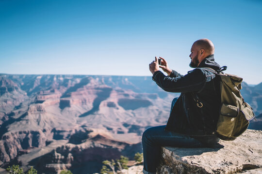Young hipster guy enjoying beautiful landscape of National park taking picture on smartphone camera,male traveler photographing scenery nature view in Grand Canyon on high mountain cliff with cellular