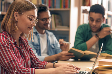 Three young students study in the school library and using laptop for researching online.