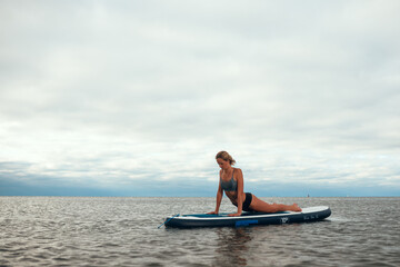 Woman practicing yoga on the paddle board in the morning