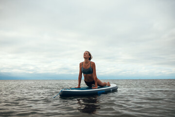 Woman practicing yoga on the paddle board in the morning