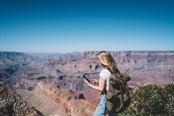 Young hipster girl checking mail on smartphone hiking in mountains on active weekend,female tourist with backpack using good mobile data connection in wild nature for communicating during tour