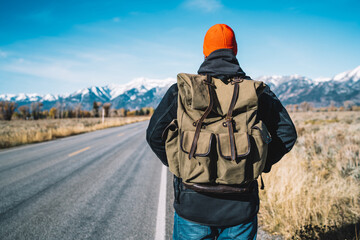 Guy wanderlust looking forward while exploring wild nature in hiking tour, back view of young male traveler standing on road and spending time for discover national park with beautiful landscape