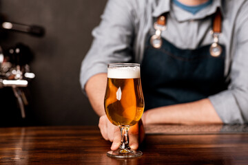 Pint of beer on bar in traditional style of pub. Guy in apron gives glass of light ale