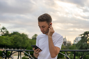 Photo of a young and attractive man with headphones listening to music in his phone in the park