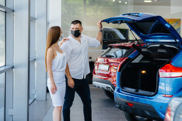 Young couple in masks selects a new vehicle and consult with a representative of the dealership in the period of the pandemic. Car sales, and life during the pandemic