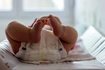 Baby girl lying on white sheet and holding her legs up in the air.Image of unrecognizable cute baby in dippers shaking feet while lying in bed,innocence concept.A cropped shot of baby feet.Copy space.