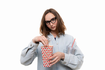 A young girl in a denim shirt holds glasses and popcorn on a white background