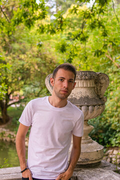 Photo of a young and attractive man with a pensitive expression next to a stone statue in the middle of nature