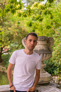 Photo of a young and attractive man with a pensitive expression next to a stone statue in the middle of nature