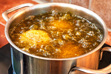 Sicily street food Arancini are frying in boiling olive oil in the pan. Italian fast food. Selective focus