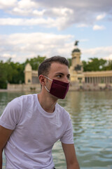 Photo of a young and attractive man wearing a face mask and sitting next to a beautiful and graan park isolated in nature