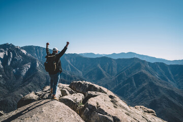 Back view of male traveler celebrating achievement of getting on mountain top destination standing...