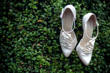 A pair of white elegant bride shoes on a green bush background