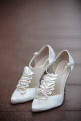 A pair of white elegant bride shoes on a brown woodenbackground