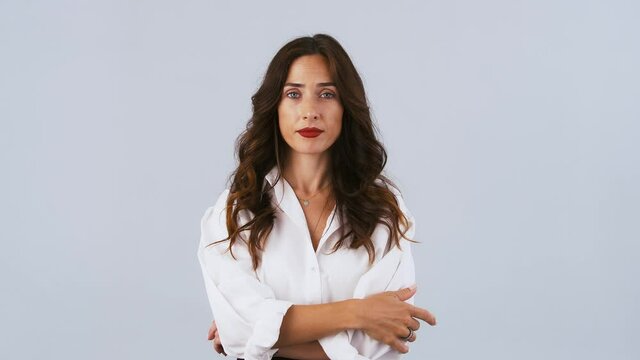 Young brunette girl in white shirt is imitating zipping her mouth shut and throwing out the key. Keep a secret. Posing on gray background. Close up