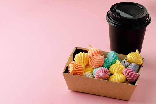 Black carton coffee cup with box of colorful meringue cookies on pink