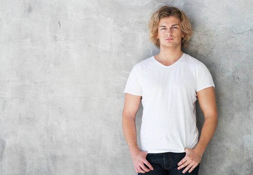 Young man, fashion model posing in white t-shirt on wall background