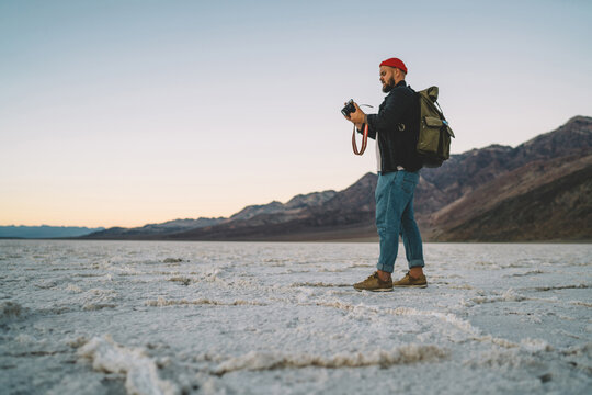 Skilled male photographer with backpack working during trip to wild lands of desert explore desolate area, hipster guy using modern camera for taking pictures of nature and landscape in death valley