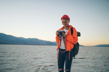 Smiling girl viewing photos on camera enjoying expedition in wild lands of Badwater national park,professional female photographer checking settings on equipment working during Death Valley trip
