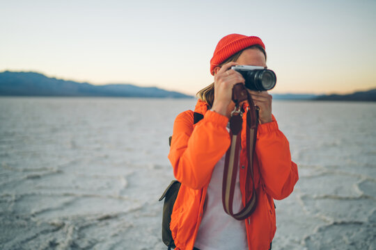 Professional female photographer working in wild environment of national park in USA with desolate arid surface, young woman making picture on digital camera during expedition in Badwater basin.
