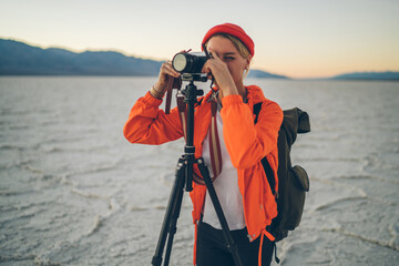 Skilled female travel photographer using tripod for shooting video of scenic locations in desert,...