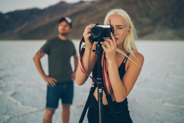 Male and female bloggers working together on shoot video of scenic view of lowest point in America,photographers making picture on modern digital camera on tripod in Badwater basin