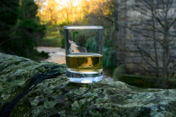 Scotch single malts or blended whisky spirits in glasses with water of river Spey on background,...