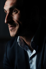 Close up portrait of a serious man 30-34 years old in a blue shirt and a dark jacket on a black background.