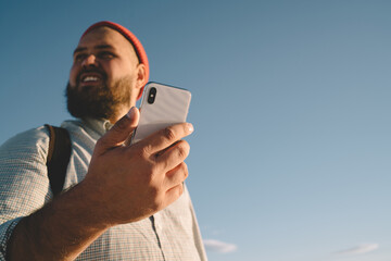 Caucasian male tourist holding modern cellphone gadget in hand and looking around during sunny day for recreation on nature, millennial blogger using digital technology for online web mobility