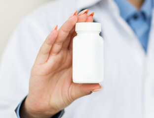 Physician medicine doctor or pharmacist sitting at worktable, holding or showing bottle of pills in hand and writing prescription on special form. Medical care, pharmacy or health insurance concept