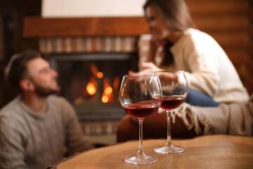Lovely couple near fireplace at home, focus on glasses with wine. Winter vacation