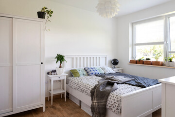 Interior of white bedroom  with double bed, window, wooden furniture and copy space on the wall. Minimalist space and scandinavian design at home. Bedding and sheets.