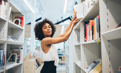 Female student reaching out book from bookshelf in library