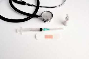 coronavirus (covid-19) vaccine concept syringe with glass container adhesive dressing, stethoscope, white background, top view