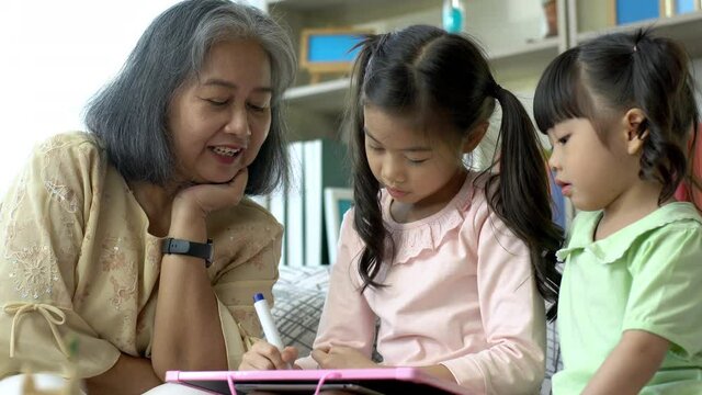 A kind and gentle Asia grandmother teaching her granddaughter to read write and drawing on a white board at home
