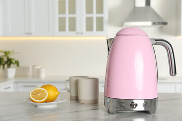 Modern electric kettle, cups and lemons on table in kitchen